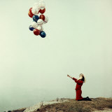 Young Woman in a Red Dress and Hat  Kneeling and Holding a Line with a Bunch of Colored Balloons