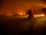 A fireman watches flames advance down a hill toward local businesses