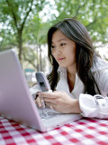 Young Woman Checks Her Laptop Computer with a Mobile Phone in Hand