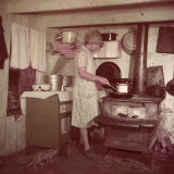 Woman Stands at Old-Fashioned Stove to Cook  Cats Prowl at Her Feet