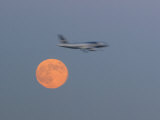 Jetliner Streaking across the Sky with a Full Red Moon in Background