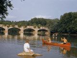 Men Paddle Canoe on Tranquil River Past Girl Perched on Rock