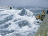 Men Paddle Narrow Channel Between Rocks and Wall Along Riverbank