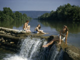 People in Bathing Suits Sit at Edge of Small Waterfall in Wide River