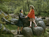 Young Couple Holds Hands While Standing on Rocks Near a Riverbank