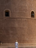 Old Omani Man Walks Beneath the Imposing Watchtower of Al Hazm Castle  Oman