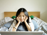 Young Chinese Woman Watches a Movie on Her Laptop Sprawled on a Bed