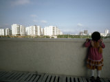 Little Girl Looks over a Wall Toward High Rises Near Hong Kong