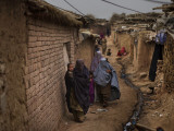 Three Afghan Refugee Women and their Children Walk in an Alley of a Poor Neighborhood in Pakistan