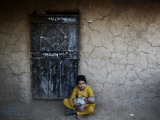 Afghan Refugee Youth Sits on the Ground Holding a Baby in Front of a Shop in Pakistan