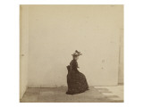 Femme assise  de profil dans une cour aux murs blancs