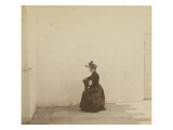 Femme assise  de profil dans une cour aux murs blancs