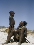 A Seated Kuvale Herdsman Beams at His Young Son Who Stands Close By