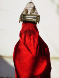 Woman Draped in Red Chadri Carries Goldfinches in a Cage on Her Head