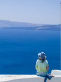 A Tourist Sits on a Stucco Wall Overlooking the Aegean Sea