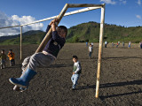 Boy Climbing Goal Post  with Corn Fields on Slopes of Acatenango Volcano in Background