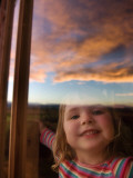 Portrait of Young Girl at Window with Reflection of Clouds at Sunset