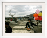 An Afghan Boy Sits on a Grave Plot and Sells Balloons and Eggs as Others Relax