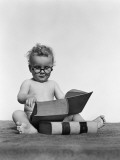 Baby Boy is Wearing Round Glasses While Reading a Very Large Book