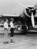 Two Boys Standing Next To Propeller Aeroplane  Holding Toy Plane