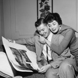 Wife Hugging Husband As He Sits in Armchair  Reading Newspaper