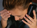 Woman Talking on Phone and Rubbing Forehead With Fingertips