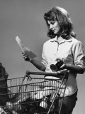 Woman Reading Shopping List Beside Grocery Cart