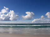 Gentle Waves and Surf Surging onto a Flat Beach under Puffy Clouds