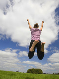 Young Woman Jumping in a Field under a Cloud-Filled Sky