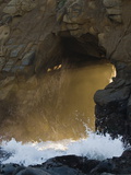 Sunset Light Beams Through a Whole in a Rock on a Rocky Beach