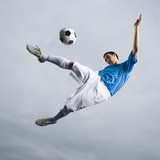 Mixed Race Teenager in Mid-Air Kicking Soccer Ball