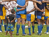 A Rugby Team in Huddle with a Child Watching Between Adults