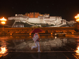 A Pedestrian in Front of the Potala Palace on a Rainy Night